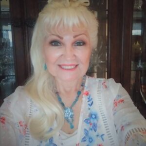 Smiling woman with blonde hair and a floral blouse.