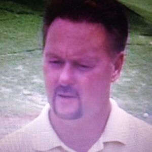 Man with short dark hair and goatee outdoors on a grassy field.