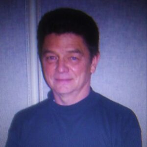 Portrait of a man in a dark shirt against a plain background.