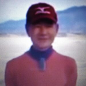 A person wearing a red cap and jacket outdoors with mountains in the background.