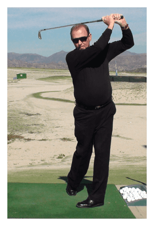 Man in black swinging a golf club on a sunny golf course.
