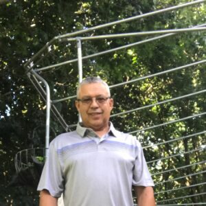 Man standing outdoors near a metal structure with greenery in the background.