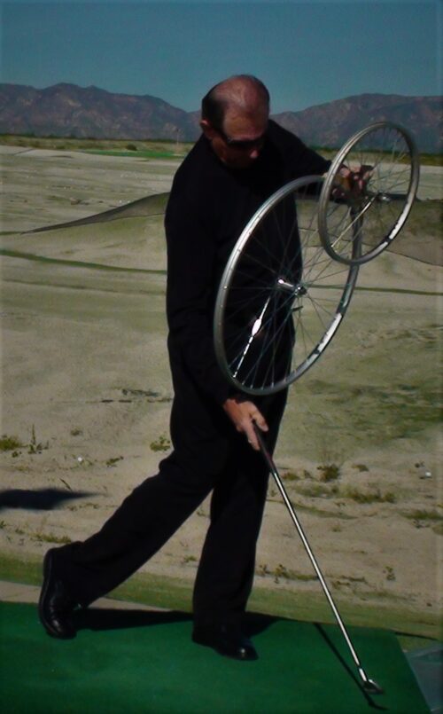 Person playing golf while holding a bicycle wheel.