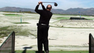 Man in black swinging a golf club on a driving range.