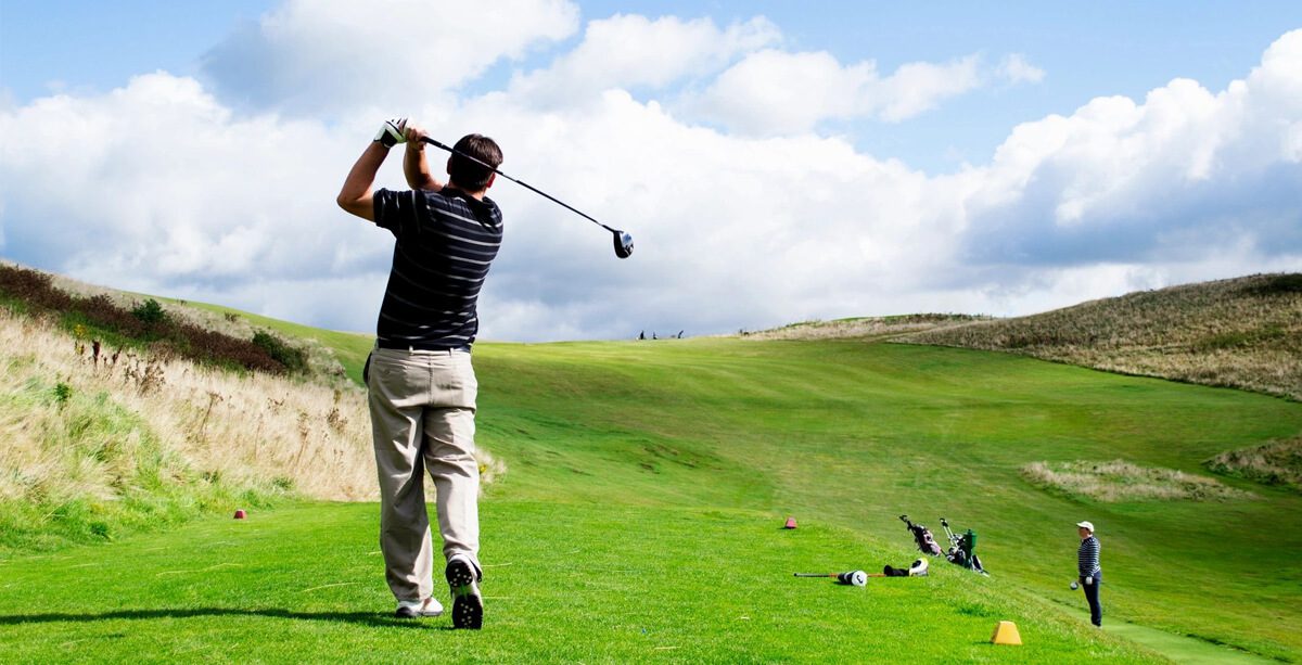 A golfer swinging on a lush green course under a partly cloudy sky.