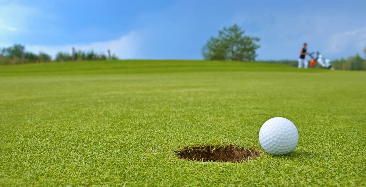 A golf ball near the hole on a green field under blue sky.