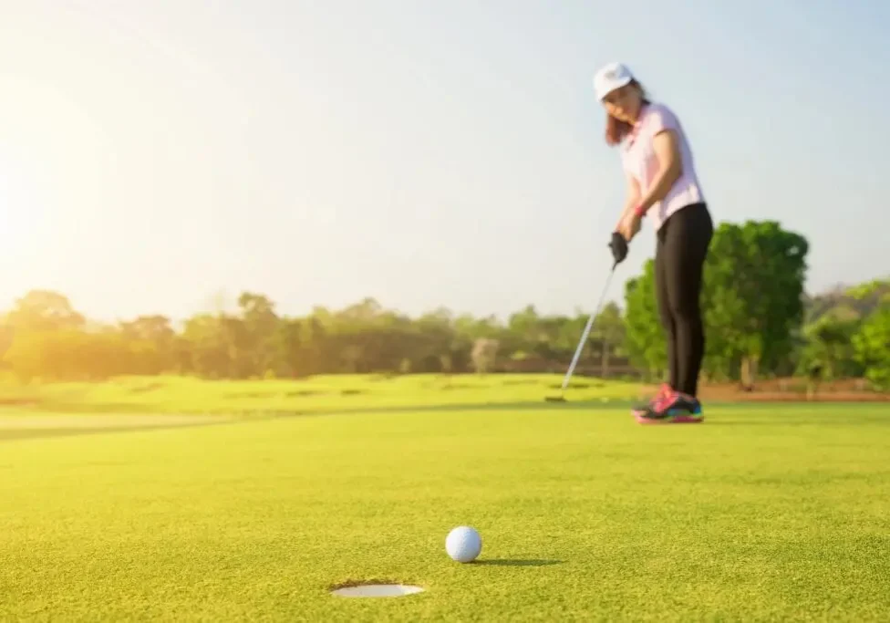 Golfer preparing to putt on a sunny green golf course.