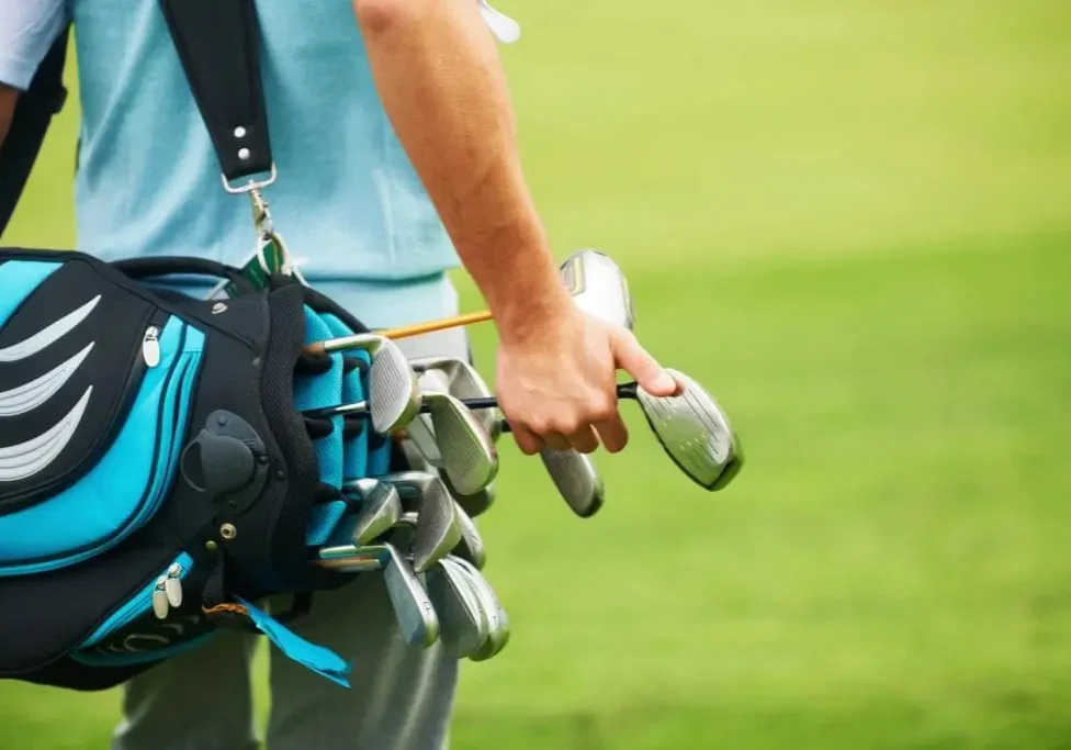 Golfer holding two golf clubs on a green golf course.