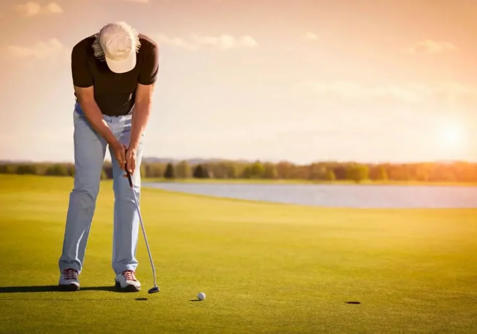 Golfer putting on a sunlit green near water.
