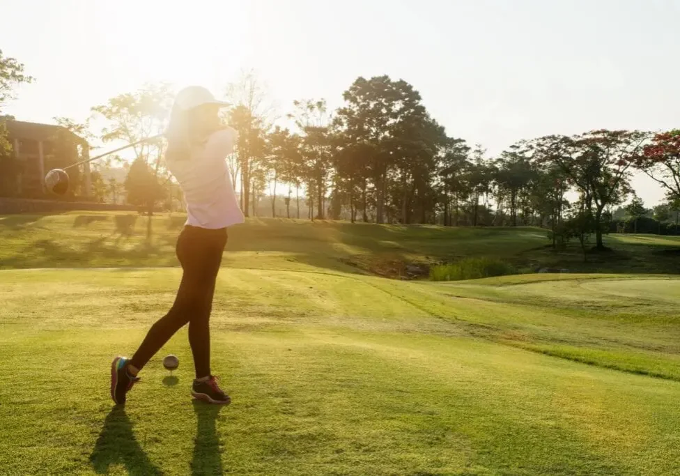 Golfer walking on a sunlit green golf course.