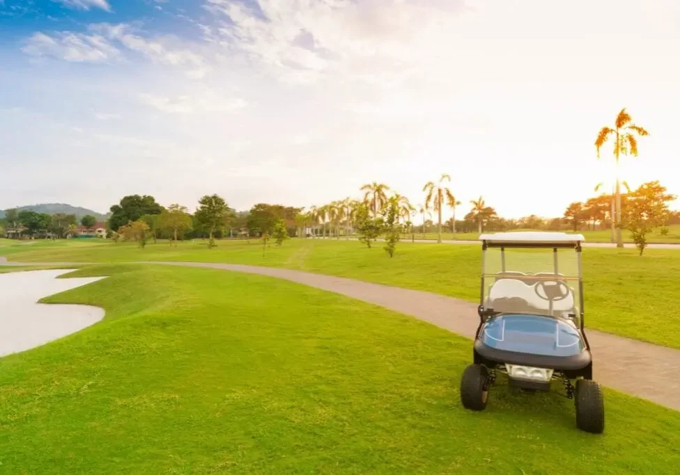 Golf cart parked on a green golf course under a clear sky.