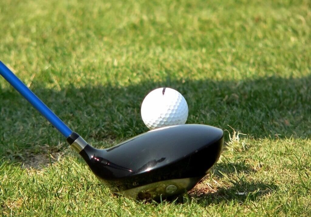 Golf ball and driver club ready for a tee shot on grass.